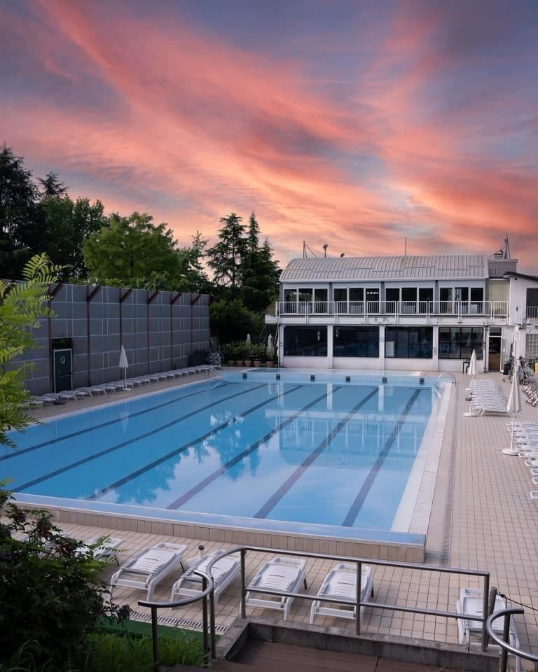 Piscina esterna New Way Fitness con corsie, lettini e cielo al tramonto